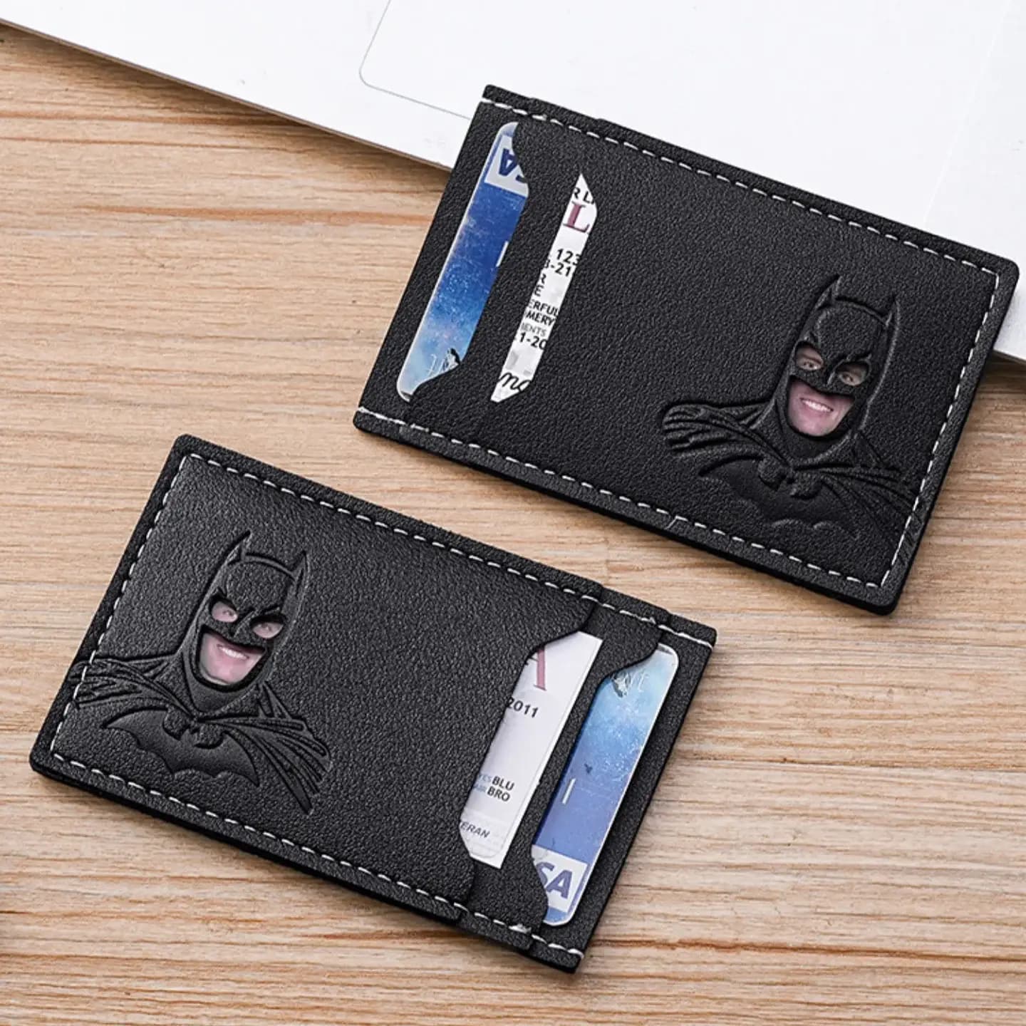 Two slim black PU card holders with cards inside, lying on a wooden desk